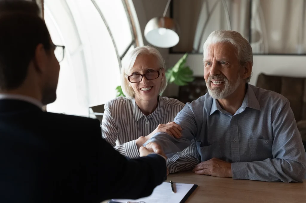 Happy grateful elderly couple of clients thanking real estate agent, lawyer, broker for help with house buying or selling