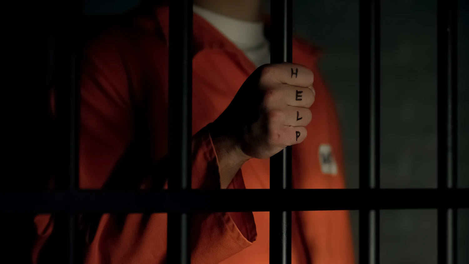 Help word written on prisoner fingers, male holding jail bars, ill treatment